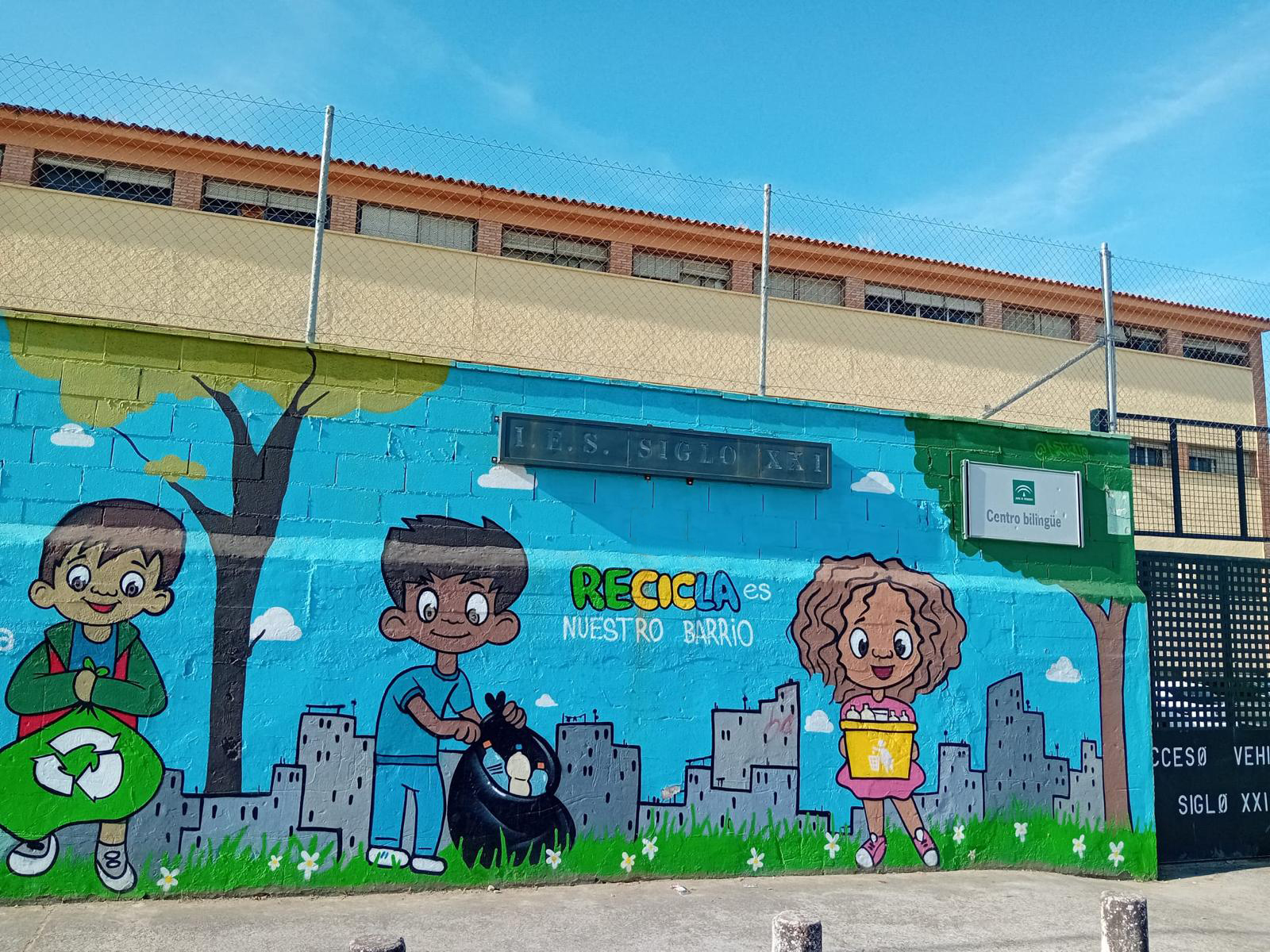 Imagen de uno de los murales del muro exterior del centro en la que se ve el nombre del centro, un cartel que indica que es un centro bilingüe y un mensaje apoyando el reciclaje